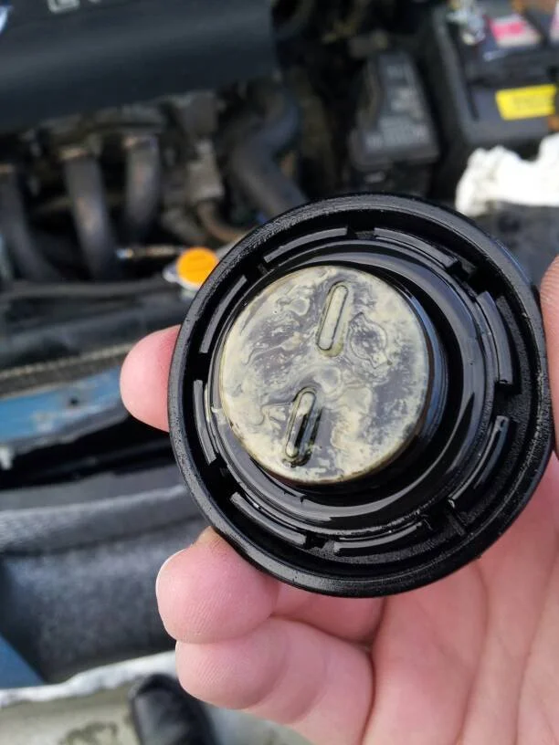 Milky, emulsified oil on an engine oil filler cap, a classic sign of a blown head gasket.